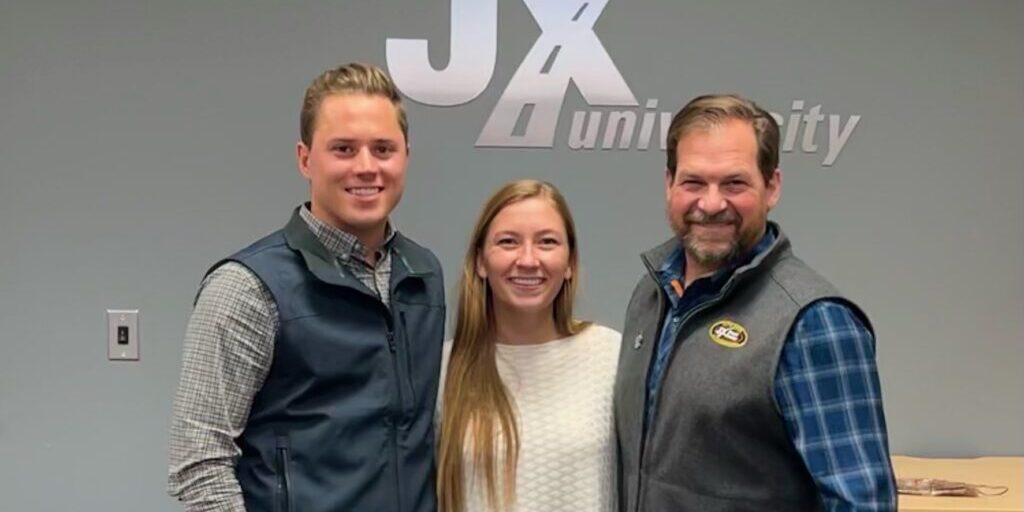 Austin Freeman, Hannah Freeman, and Eric Jorgensen in front of JX Enterprises logo